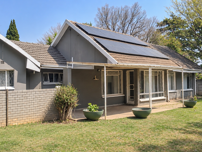 Rear view of the house featuring a tiled roof with installed solar panels, a covered patio area, and a brick boundary wall.