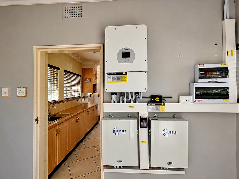 A clean utility space featuring a modern solar inverter and dual lithium-ion battery backup system with a clear view into the adjacent kitchen.