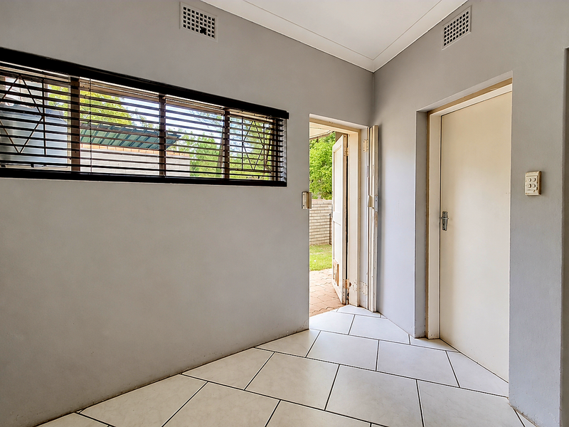 A clean utility space featuring tiled flooring, an installed solar inverter system, electrical distribution board, and direct access to the exterior.