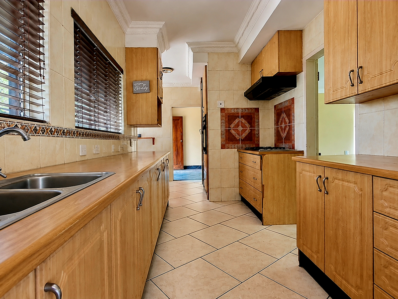 A functional kitchen featuring wooden cabinetry, tiled splashbacks, a double basin sink, and built-in cooking appliances with tiled flooring throughout.