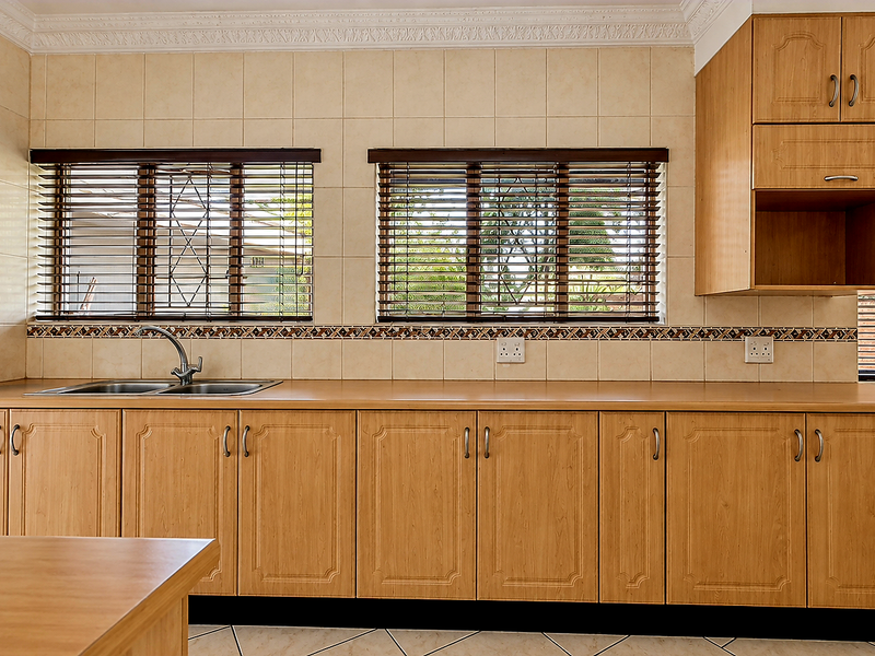 A functional kitchen featuring light wood-look cabinetry, tiled backsplash, and ample counter space with a double sink and large windows.