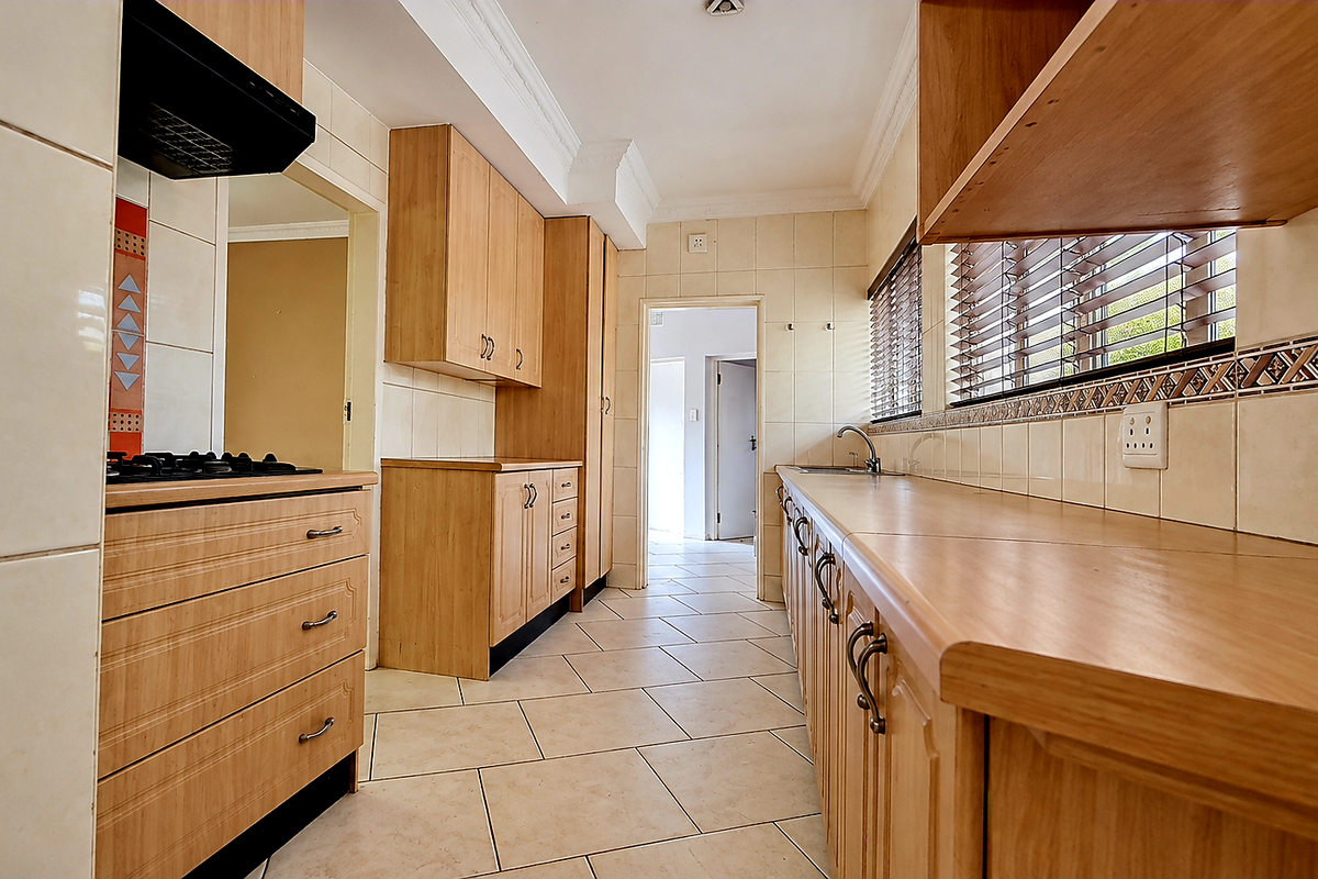 A functional kitchen featuring light wood cabinetry, laminate countertops, a gas hob with extractor, and tiled flooring, offering a clean and practical workspace.