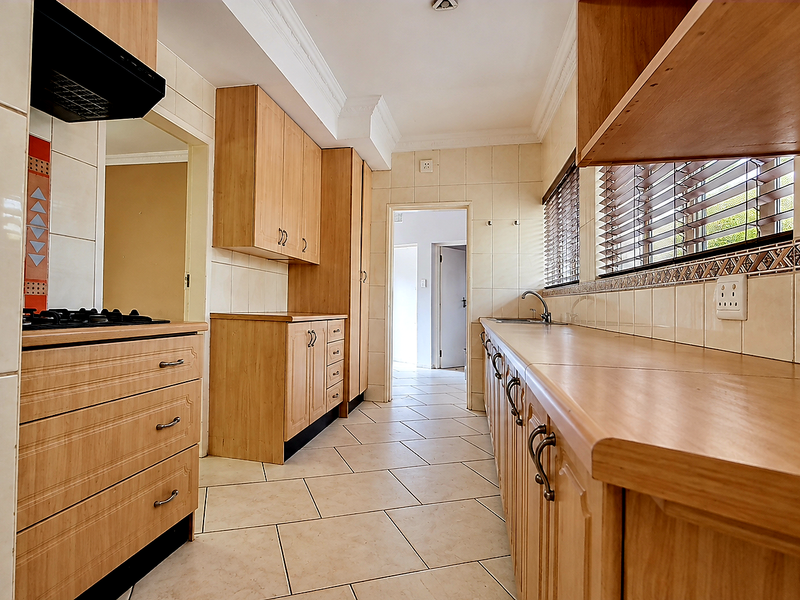 A functional kitchen featuring light wood cabinetry, laminate countertops, a gas hob with extractor, and tiled flooring, offering a clean and practical workspace.