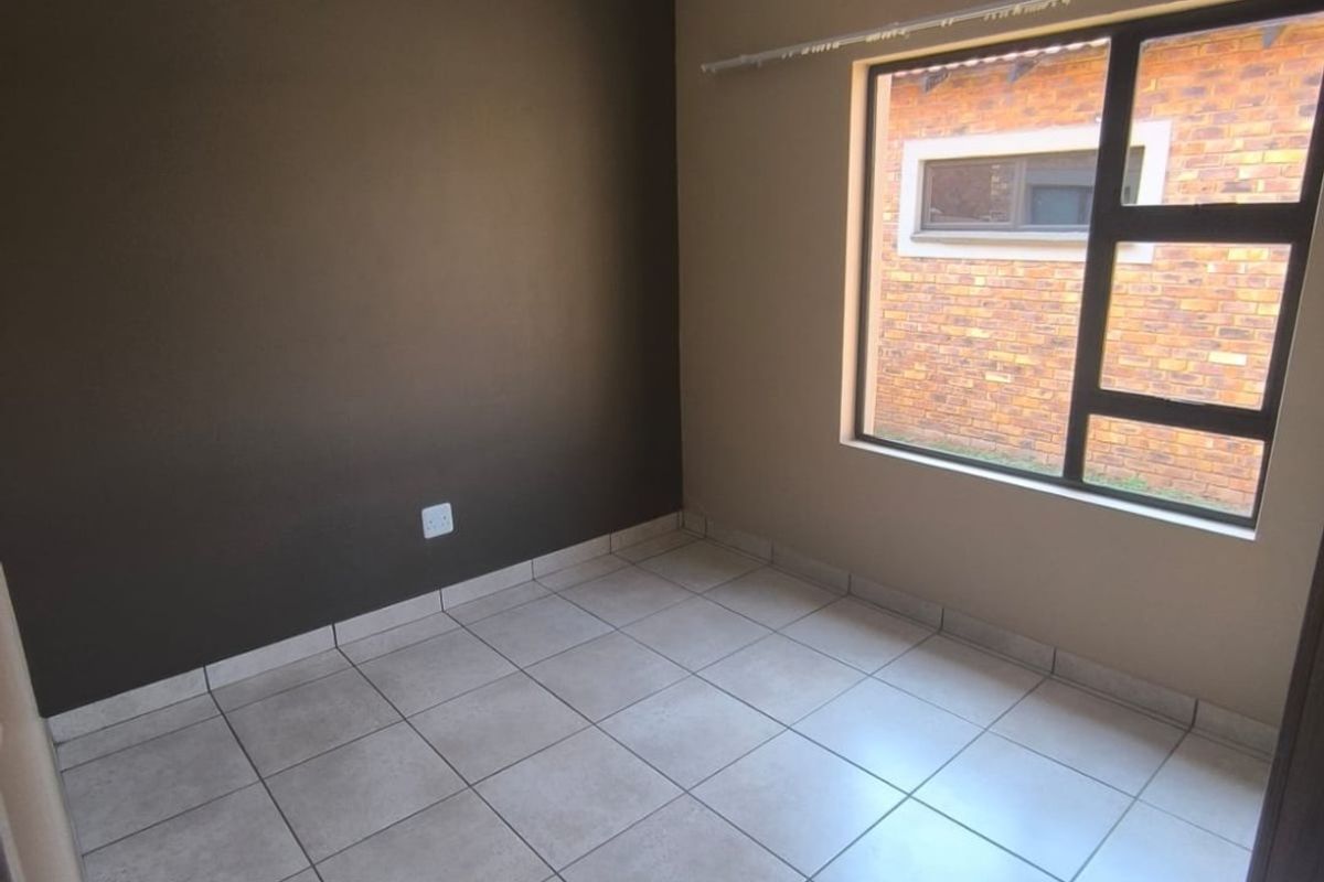 An empty bedroom featuring neutral tiled flooring, a dark accent wall, and an aluminium-framed window providing natural light.