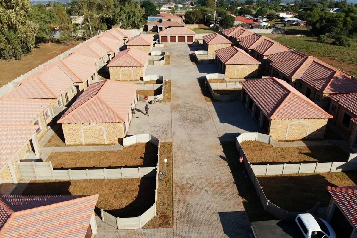 Aerial view of a commercial residential complex featuring multiple brick units with tiled roofs, paved driveways, and individual enclosed garden spaces.