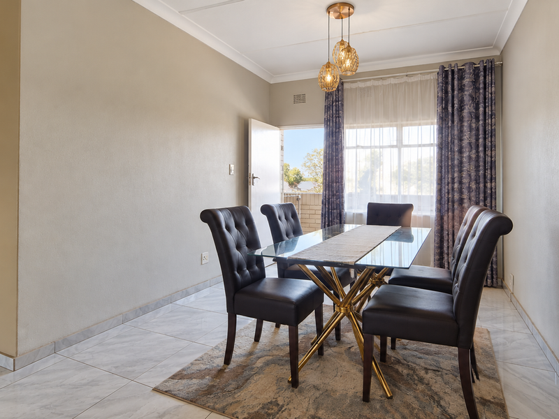 A bright dining room featuring neutral walls, polished tile flooring, and a modern pendant light fixture, with direct access to an outdoor area.