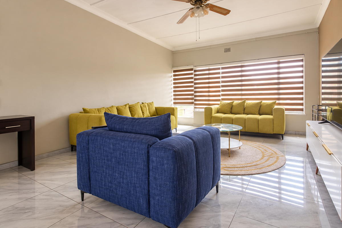 Spacious living room featuring modern tiled flooring, a ceiling fan, and large windows with adjustable venetian blinds for natural light control.