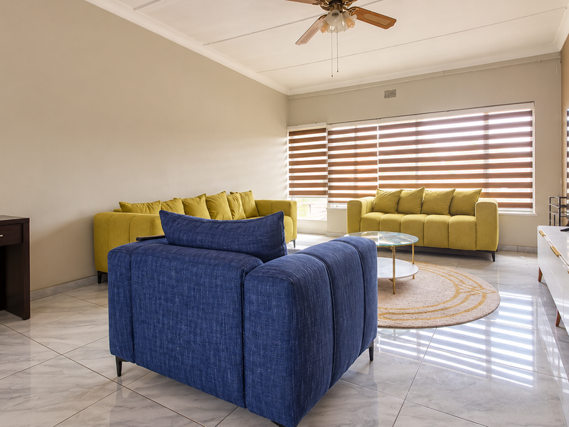 Spacious living room featuring modern tiled flooring, a ceiling fan, and large windows with adjustable venetian blinds for natural light control.