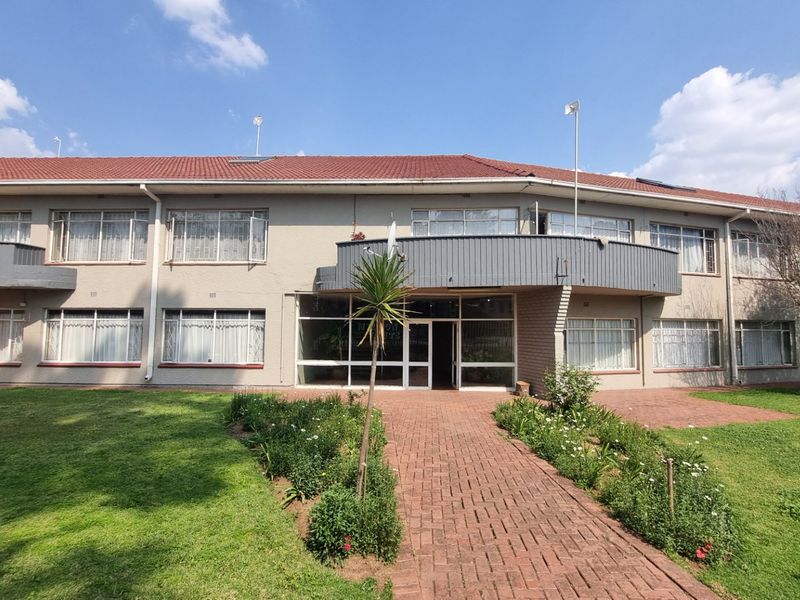 Rear view of the apartment building featuring a brick paved walkway, landscaped garden, and upper-level balconies with sliding glass doors.