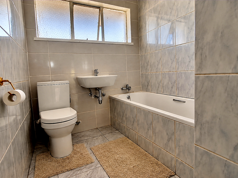 A functional bathroom featuring a bathtub, wall-mounted basin, and toilet, finished with marble-effect wall and floor tiles.