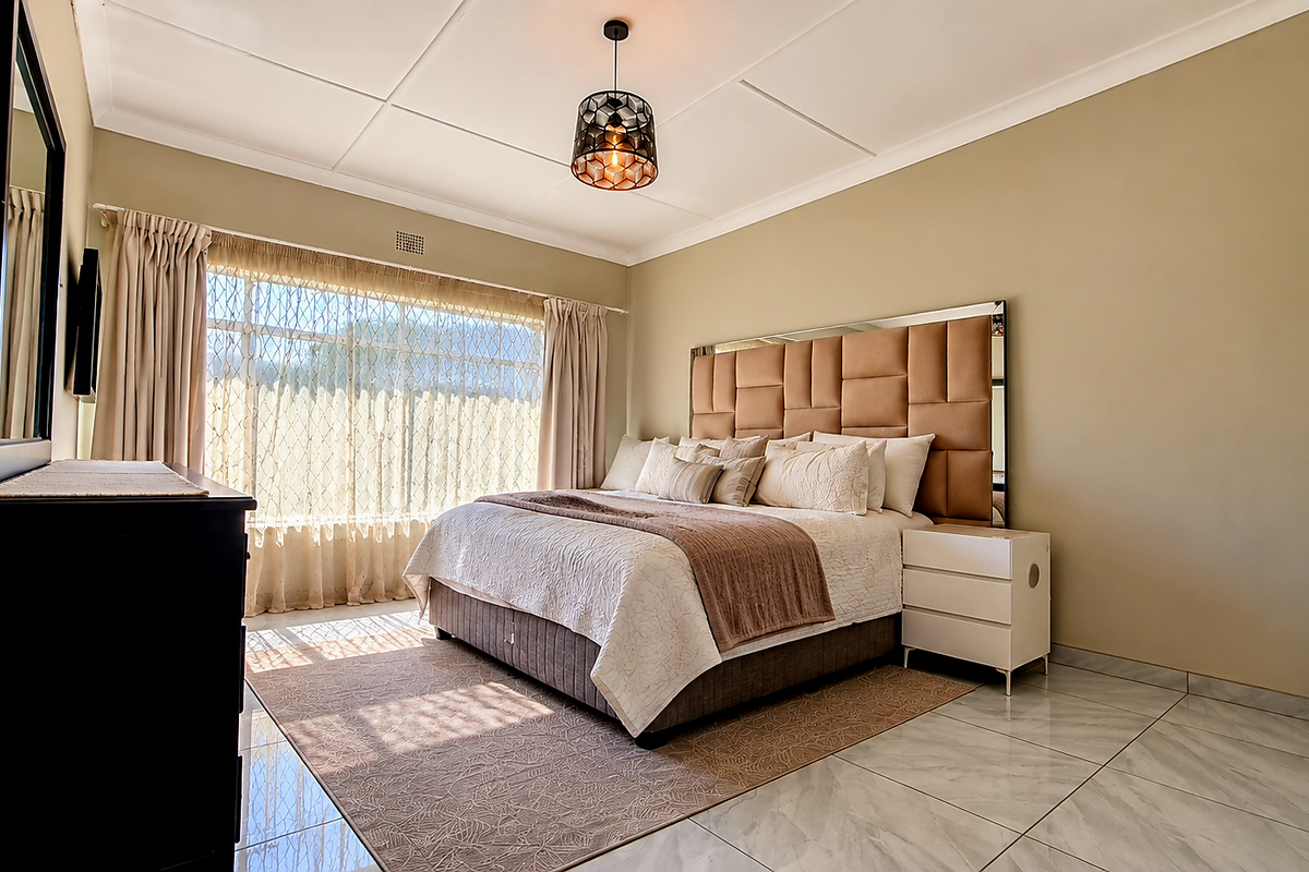 A well-maintained bedroom featuring neutral wall tones, large windows with natural light, and polished tiled flooring.