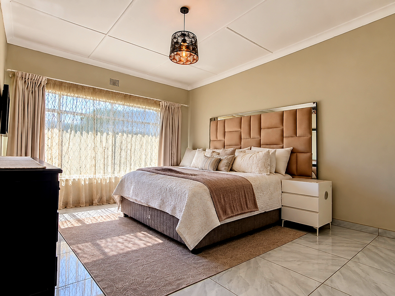 A well-maintained bedroom featuring neutral wall tones, large windows with natural light, and polished tiled flooring.