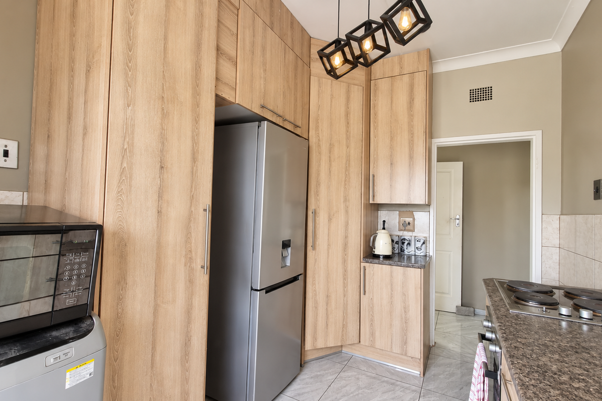 A functional kitchen featuring light wood-grain cabinetry, stone-look laminate countertops, an integrated electric hob, and tiled flooring.