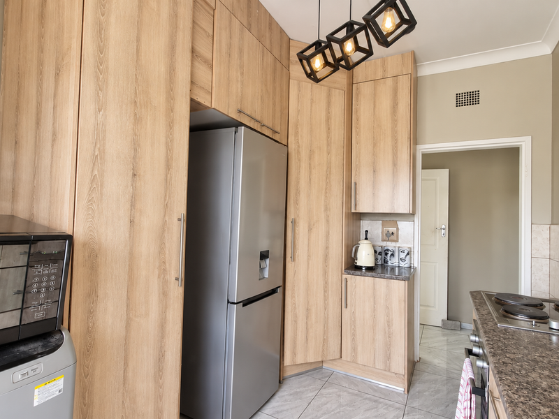 A functional kitchen featuring light wood-grain cabinetry, stone-look laminate countertops, an integrated electric hob, and tiled flooring.