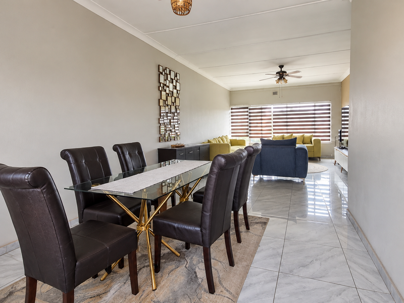 Spacious open-plan living and dining area featuring polished tiled flooring, a ceiling fan, and large windows with modern roller blinds.
