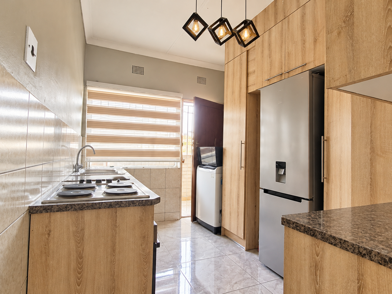 A modern kitchen featuring light wood-finish cabinetry, laminate countertops, an electric hob, tiled backsplash, and sleek tiled flooring.