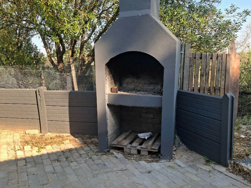 Outdoor patio area featuring a built-in braai and paved flooring, enclosed by precast concrete walling and timber fencing.