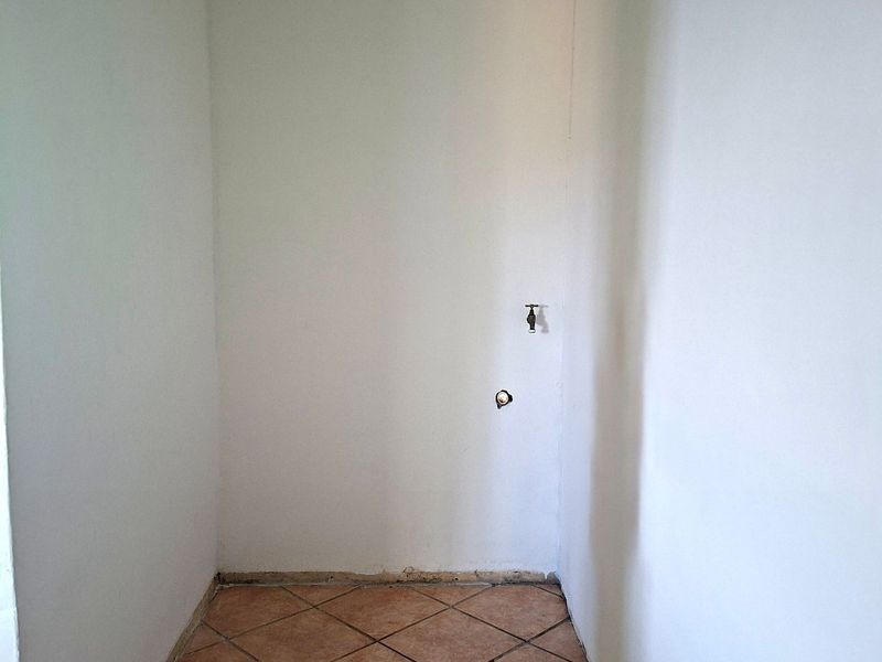 A small, empty utility or laundry space featuring tiled flooring, a wall-mounted water tap, and a drainage point, ready for renovation or appliance installation.