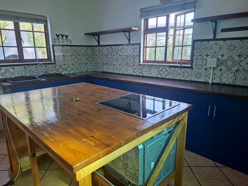 A rustic-style kitchen featuring blue cabinetry, patterned tiled splashbacks, wooden countertops, and a central island with an integrated induction hob.