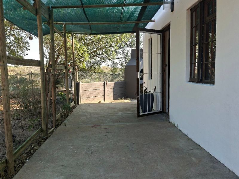 Covered outdoor patio area featuring a concrete floor, timber pergola with shade cloth, and a built-in braai, providing a functional space for outdoor entertaining.