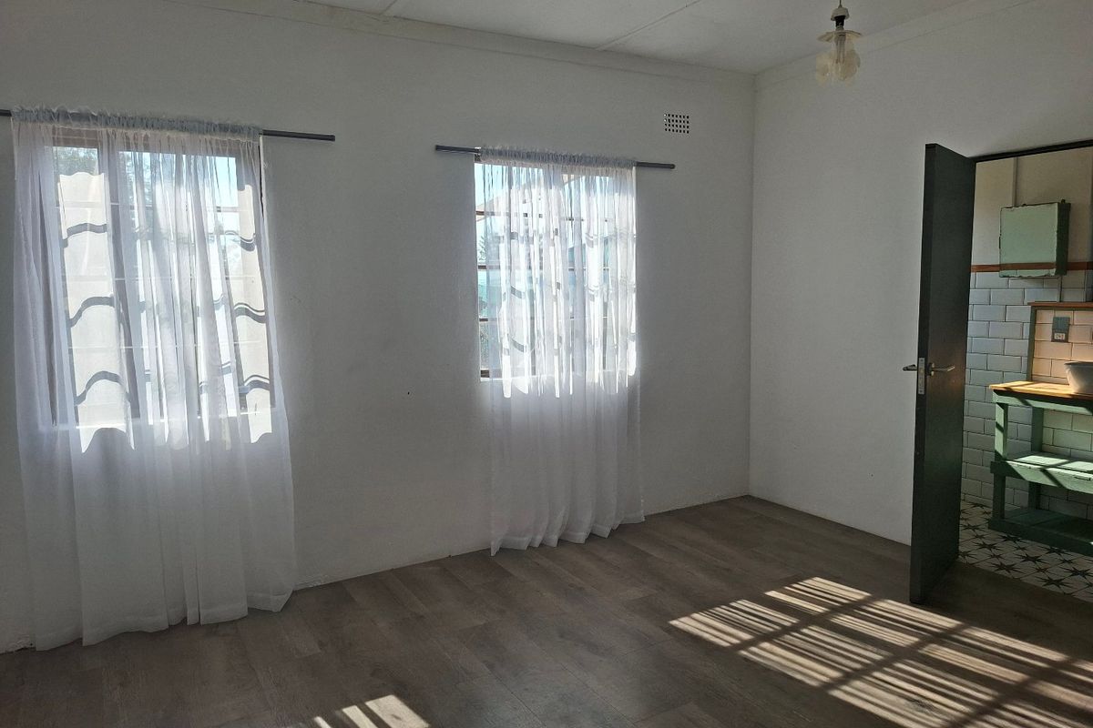 A bright, empty bedroom featuring laminate flooring and natural light, with an adjacent view into a tiled bathroom area.