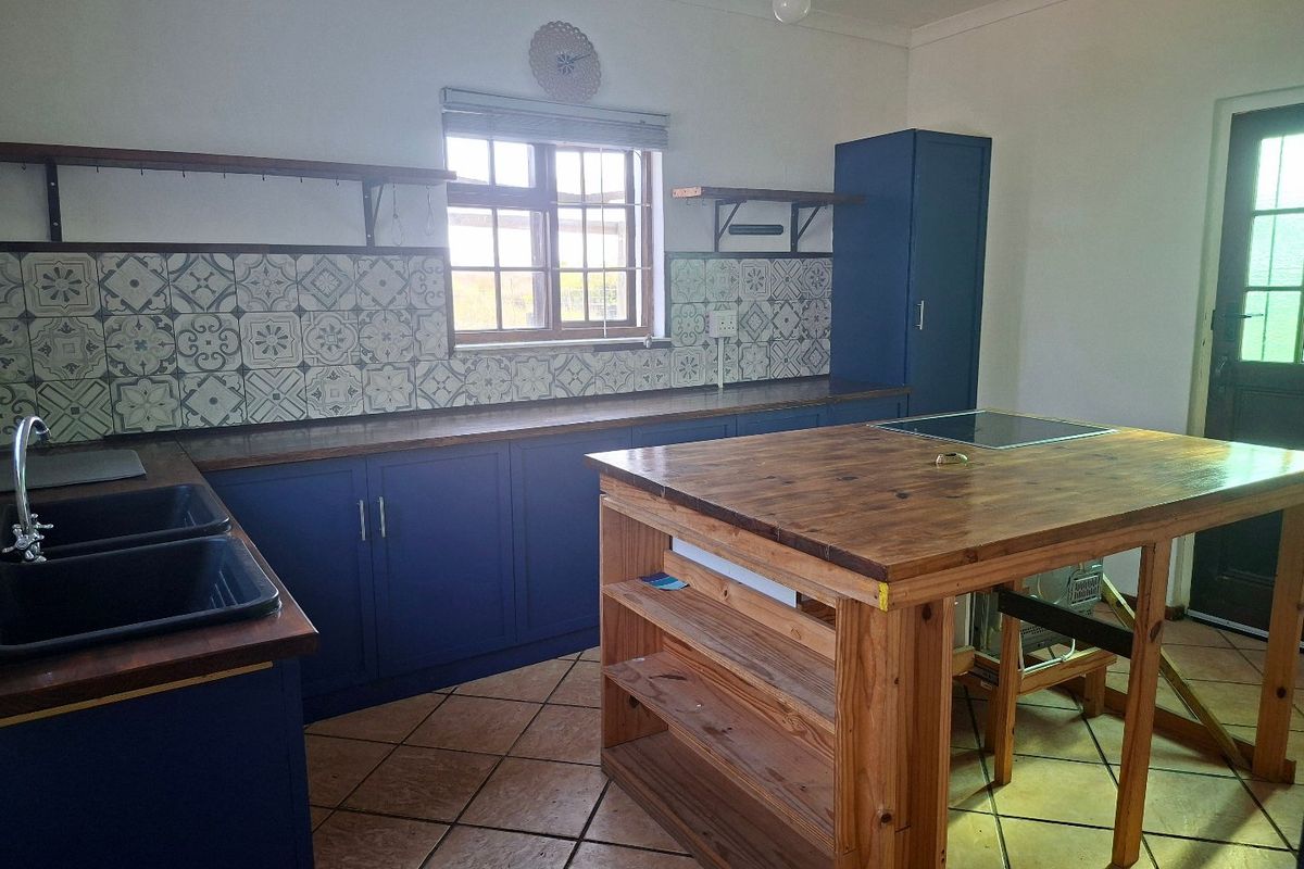 A kitchen featuring blue cabinetry, wooden countertops, a central island with a built-in hob, and decorative patterned tile backsplash.