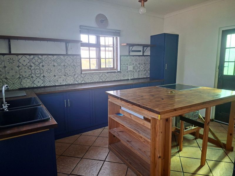 A kitchen featuring blue cabinetry, wooden countertops, a central island with a built-in hob, and decorative patterned tile backsplash.