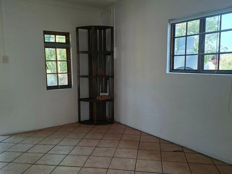 An empty living room featuring tiled flooring, a ceiling fan, and grid-pattern windows, requiring floor repairs.