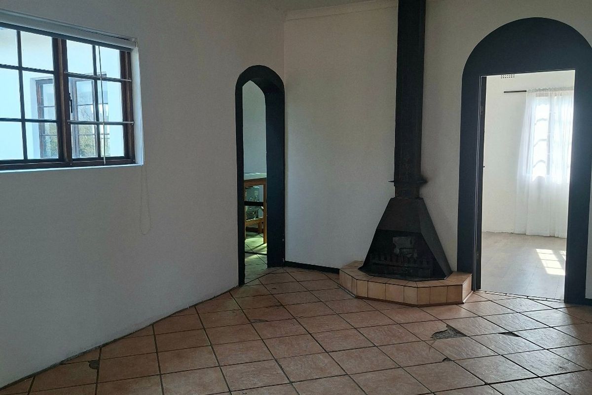 An empty living room featuring a freestanding fireplace, tiled flooring with visible damage, and arched doorways leading to adjacent rooms.