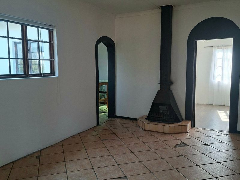 An empty living room featuring a freestanding fireplace, tiled flooring with visible damage, and arched doorways leading to adjacent rooms.