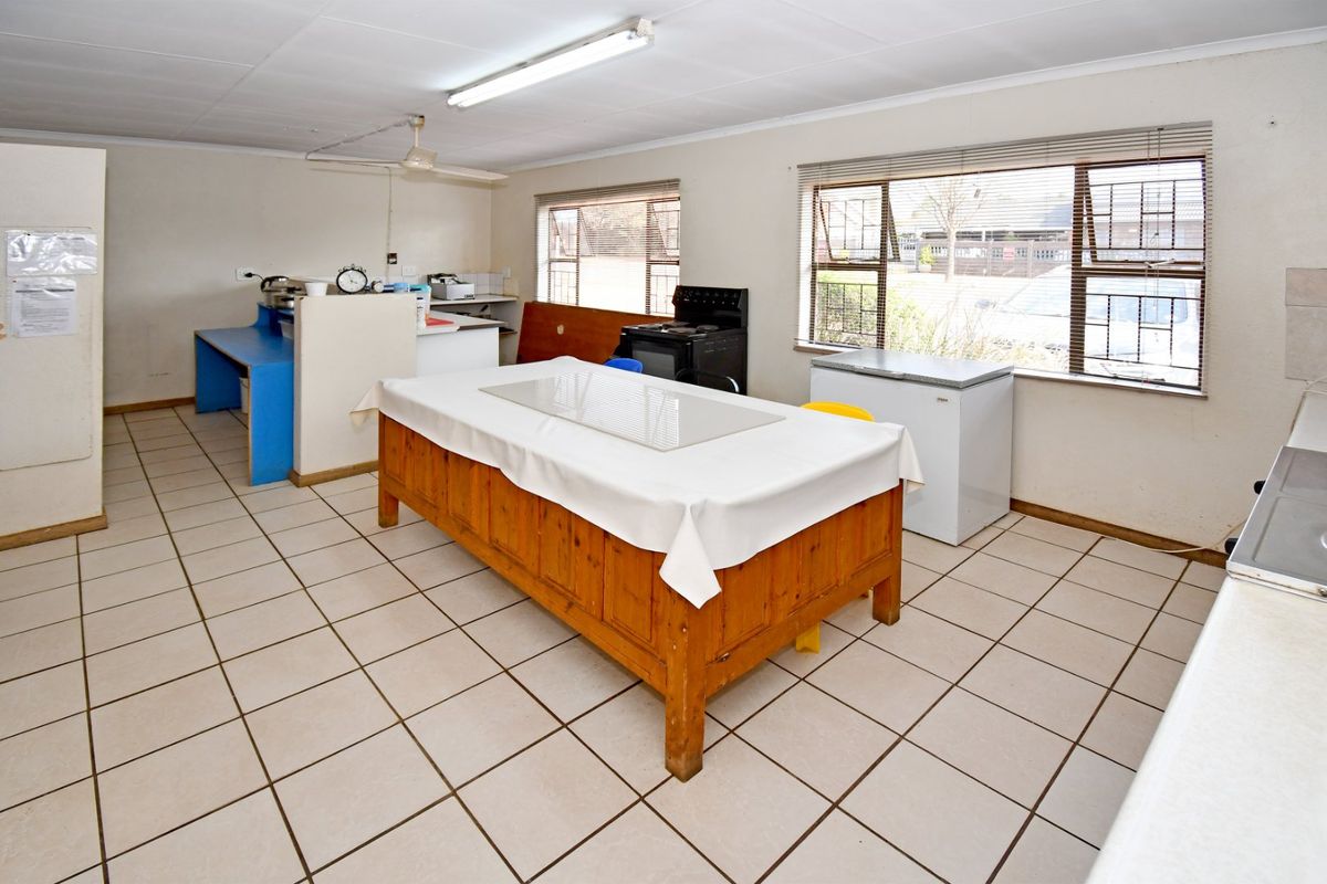 A functional kitchen area featuring tiled flooring, fluorescent lighting, and large windows with venetian blinds, offering a practical layout for commercial use.