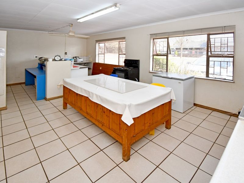 A functional kitchen area featuring tiled flooring, fluorescent lighting, and large windows with venetian blinds, offering a practical layout for commercial use.