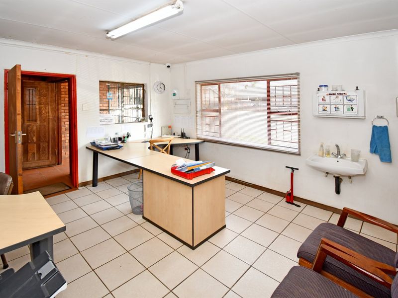 Functional commercial office space featuring ceramic tiled flooring, built-in desk configuration, wall-mounted basin, and natural light through large windows.