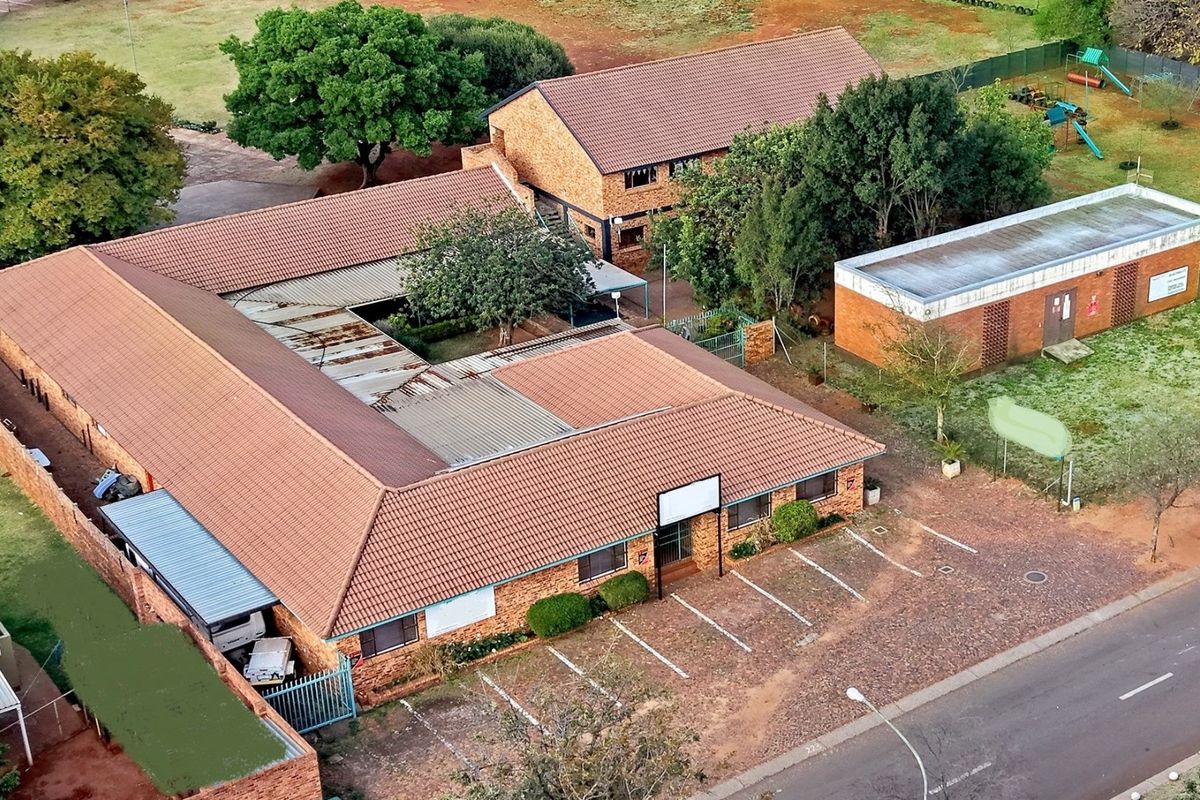 Aerial view of a commercial property complex featuring multiple brick buildings, tiled roofing, and an adjacent paved parking area.