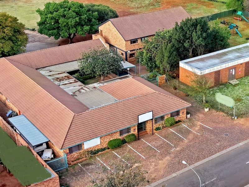 Aerial view of a commercial property complex featuring multiple brick buildings, tiled roofing, and an adjacent paved parking area.