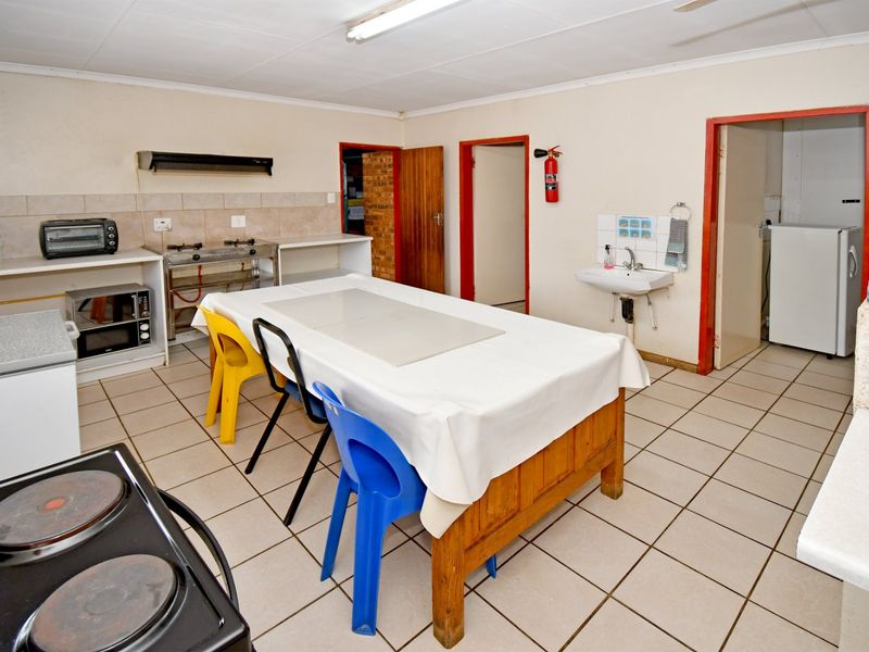 A functional commercial kitchen area featuring tiled flooring, a wall-mounted basin, and basic food preparation surfaces with integrated extractor fan.