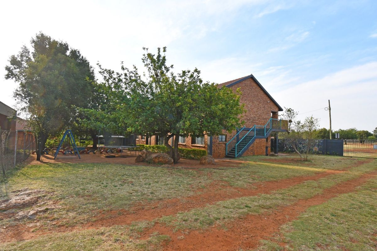 Rear view of a face brick commercial building featuring an external metal staircase and surrounding landscaped grounds with mature trees.