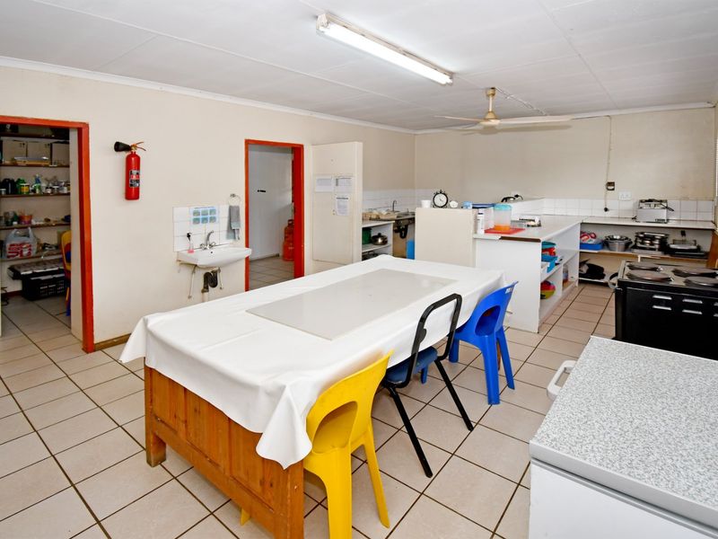 Functional commercial kitchen space featuring tiled flooring, built-in cabinetry, a wall-mounted basin, and basic utility lighting, suitable for food preparation or staff use.