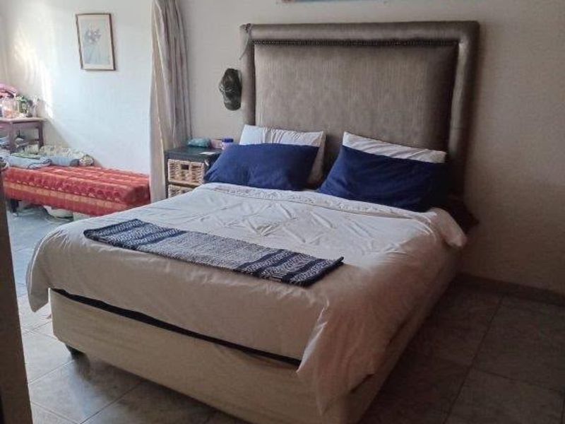 A bedroom featuring tiled flooring and recessed ceiling lighting, with an adjacent space visible through an open doorway.