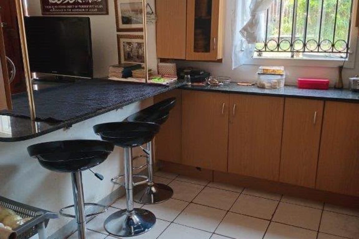 A functional kitchen featuring laminate cabinetry, granite countertops, a breakfast bar, and ceramic tiled flooring with security bars on the window.
