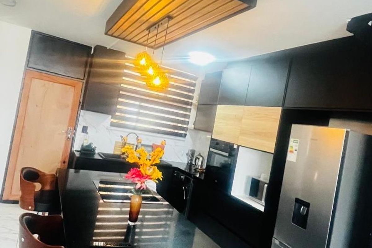 Modern kitchen featuring sleek black cabinetry, a central island with stone countertops, integrated appliances, and a stylish suspended ceiling feature with pendant lighting.