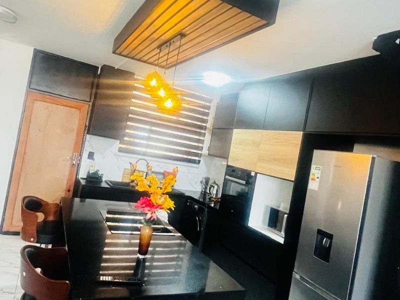 Modern kitchen featuring sleek black cabinetry, a central island with stone countertops, integrated appliances, and a stylish suspended ceiling feature with pendant lighting.