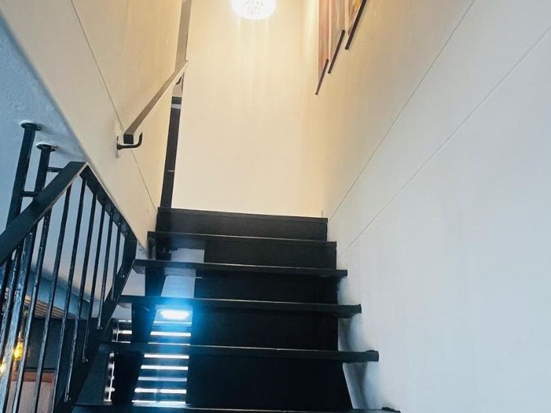 A staircase with black painted treads and a metal handrail leading to an upper level, illuminated by a modern pendant light.