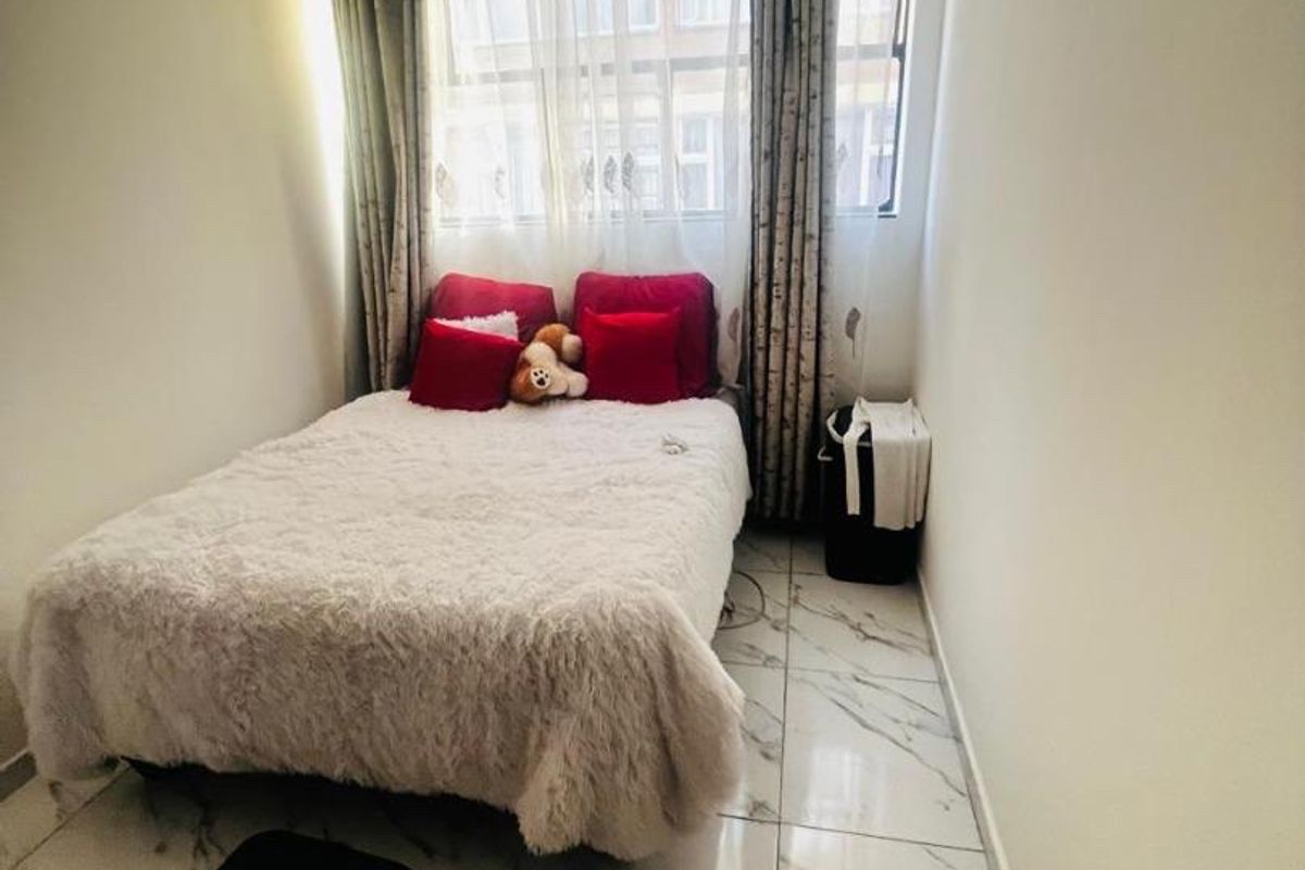 A compact bedroom featuring marble-look floor tiles and a window with curtain fixtures.