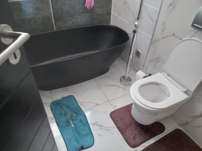 Modern bathroom featuring a sleek black freestanding bathtub, white marble-effect wall tiles, and a standard toilet.