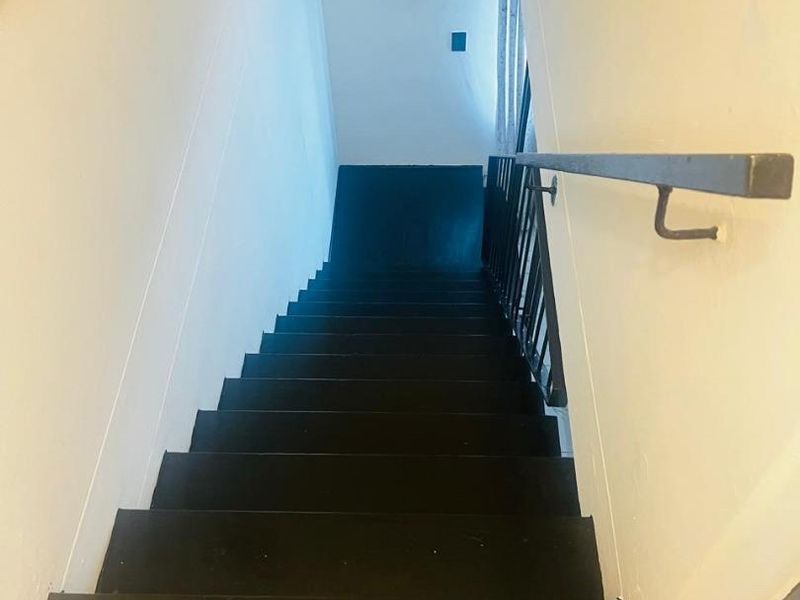 A staircase with dark painted treads and a metal handrail, leading down to a lower level with tiled flooring.
