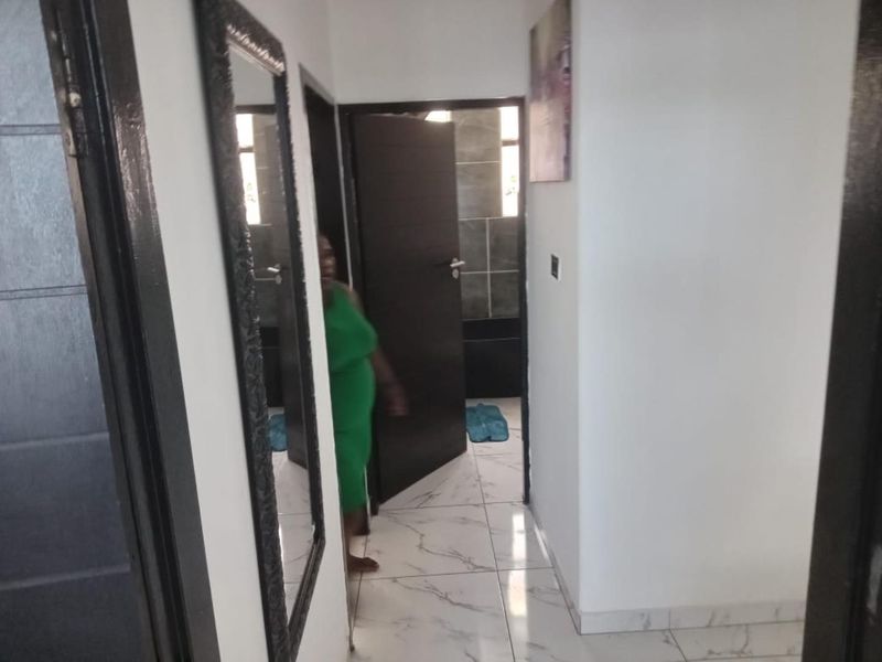 A bright hallway featuring modern white marble-look floor tiles and dark wood-finish internal doors leading to adjacent rooms.