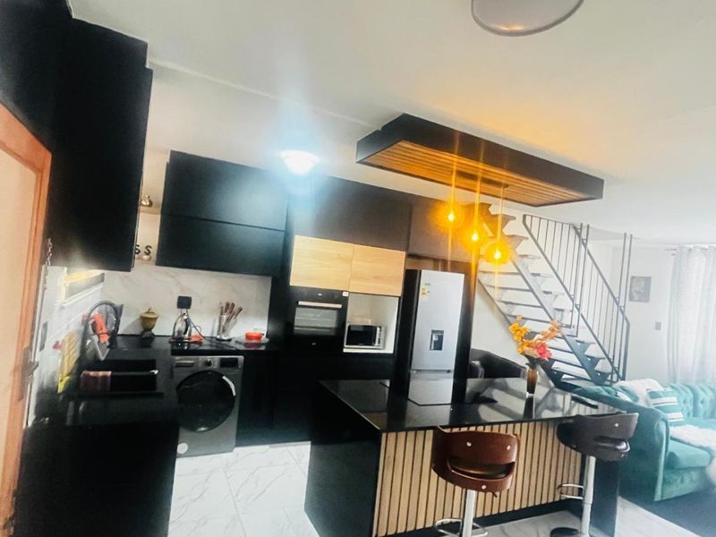 Modern open-plan kitchen featuring sleek black cabinetry, a central island, and an adjacent staircase, creating a contemporary living space.