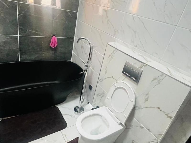 Modern bathroom featuring a sleek black freestanding bathtub, wall-hung toilet with concealed cistern, and elegant marble-effect tiling throughout.