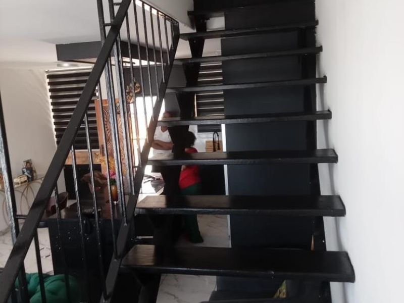 A staircase with a black metal balustrade and dark painted treads, leading to an upper level in an apartment with tiled flooring.